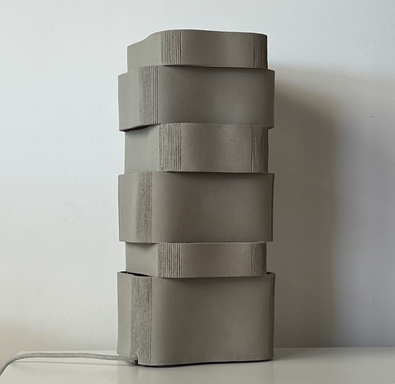 The Too 60-2 Table Lamp in Ceramic by Katia Langeard features a stacked geometric matte gray design, resembling four offset rectangular blocks, making it a perfect modern bedside lamp.