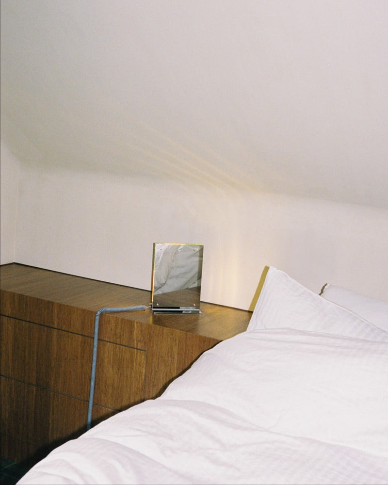 Flat Light table lamp on walnut nightstand beside white bedding