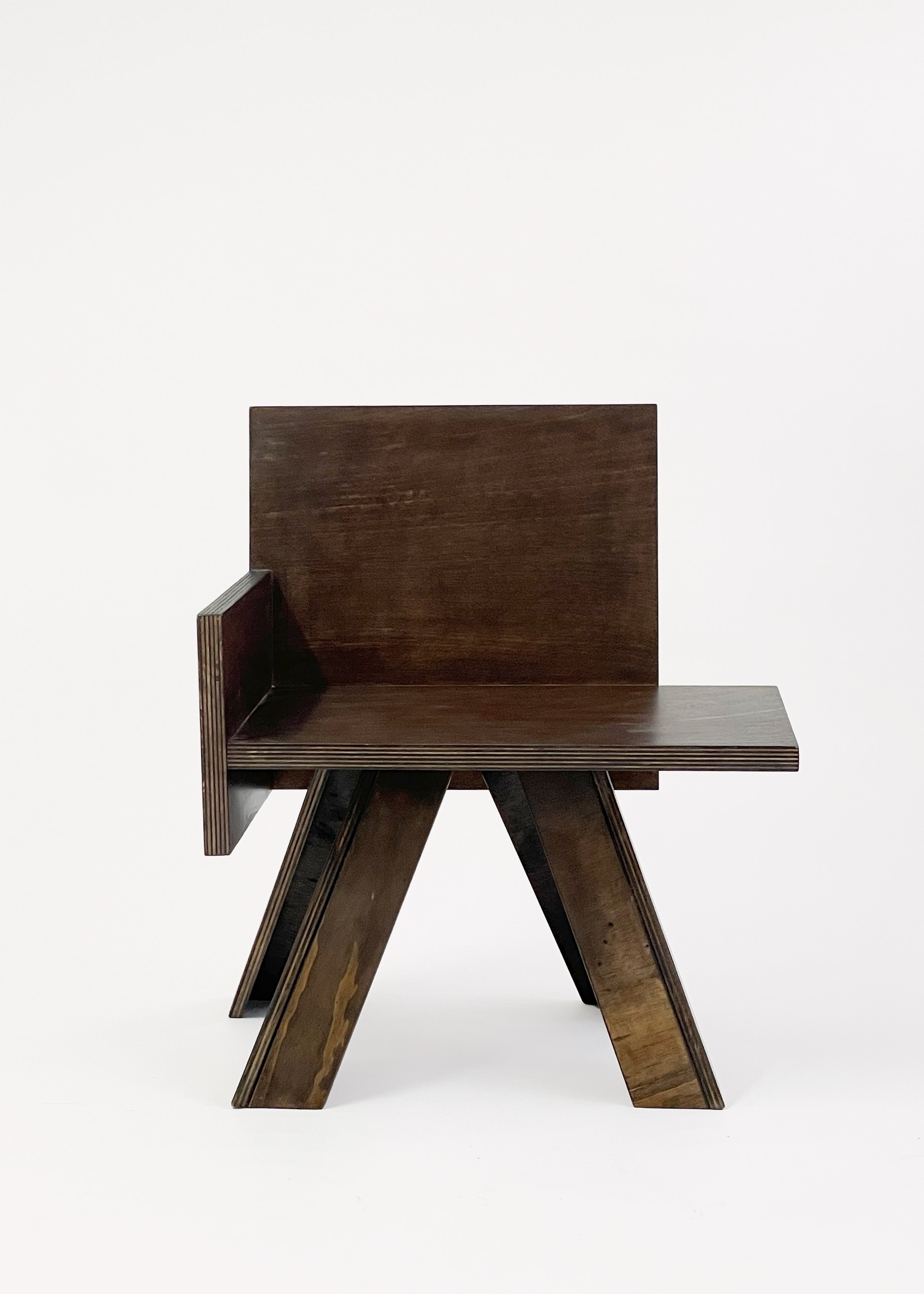 The End Table Chair by GOONS is a modern wooden chair with a dark finish, flat backrest, single left armrest, and angular splayed legs—an artisanal GOONS piece set against a plain white background.