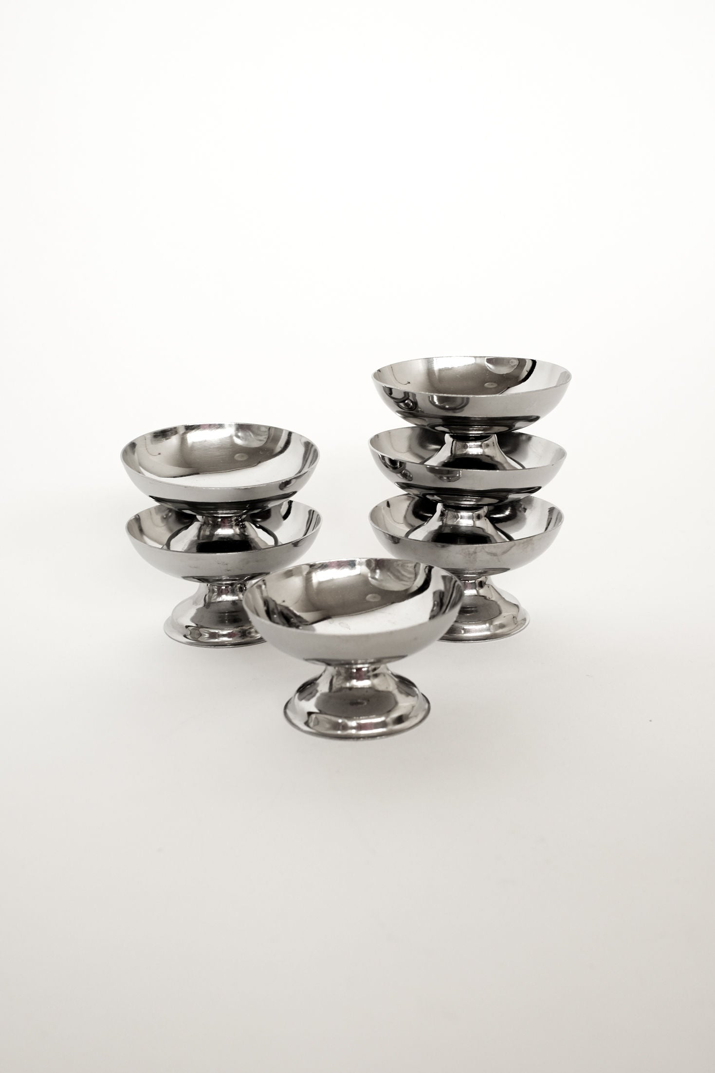 The Set of Six Ice Coupes by septembre studios features six silver metal dessert bowls, stacked in pairs with one displayed separately, elegantly presented against a plain white background.