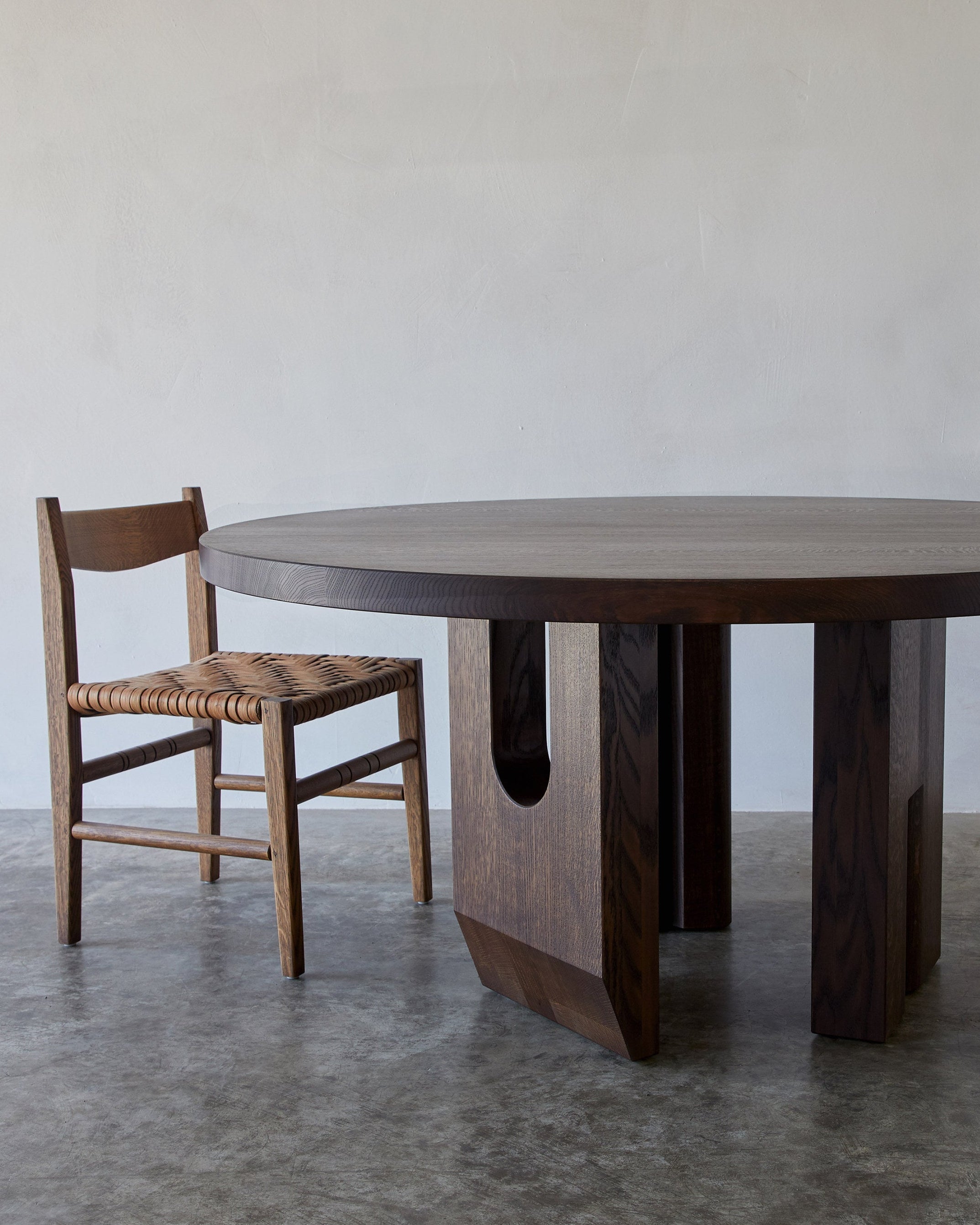 Tulia Round Dining Table — side angle showing dark wood and woven chair