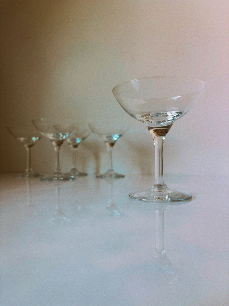 Clear Art Deco cocktail glasses set with elegant stems on reflective surface