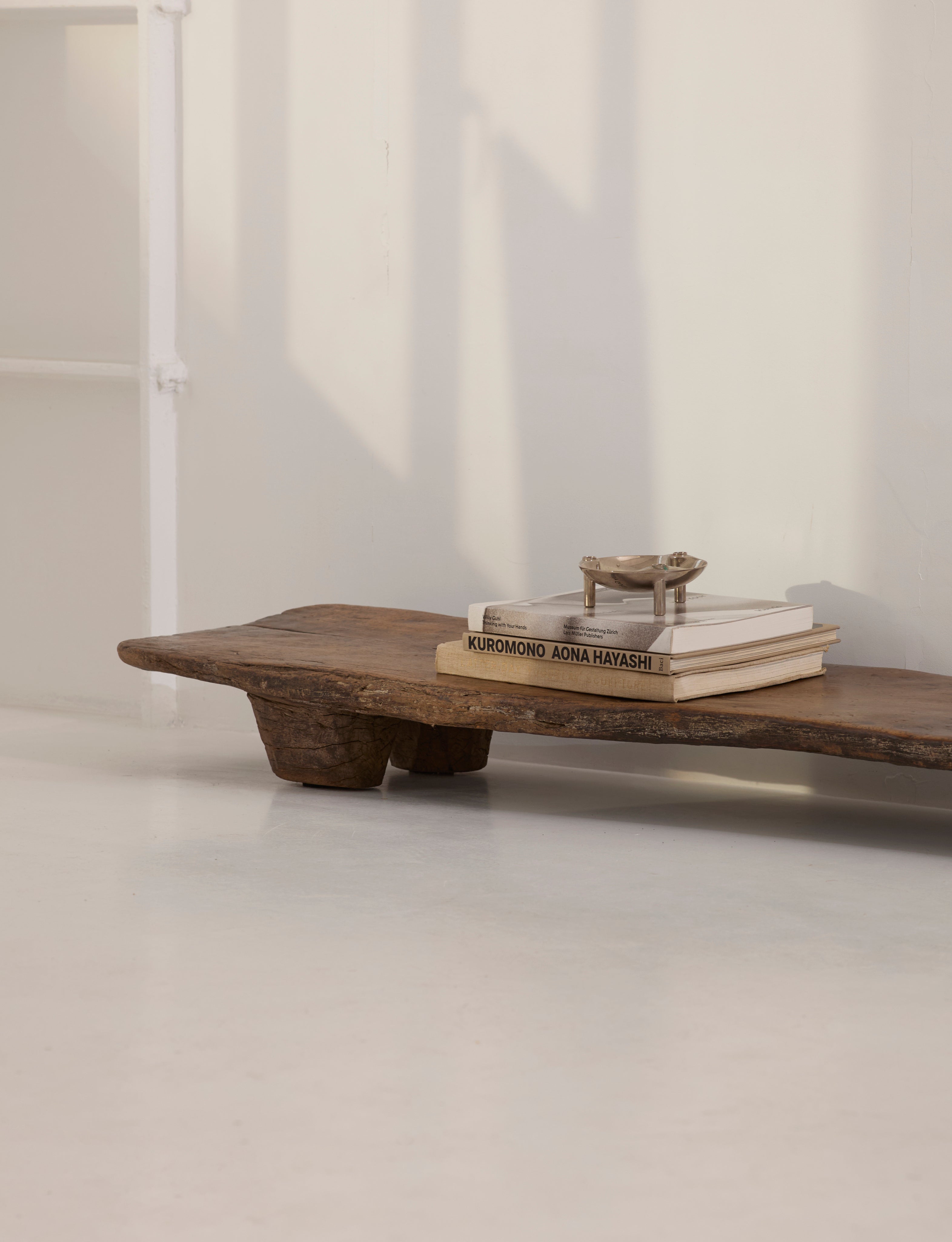 Carved Senufo Bench in Wood — side angle with stacked books on top