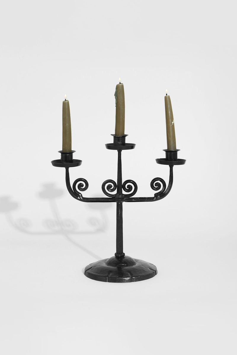 Black wrought iron candelabra with decorative spiral arms holding three candles