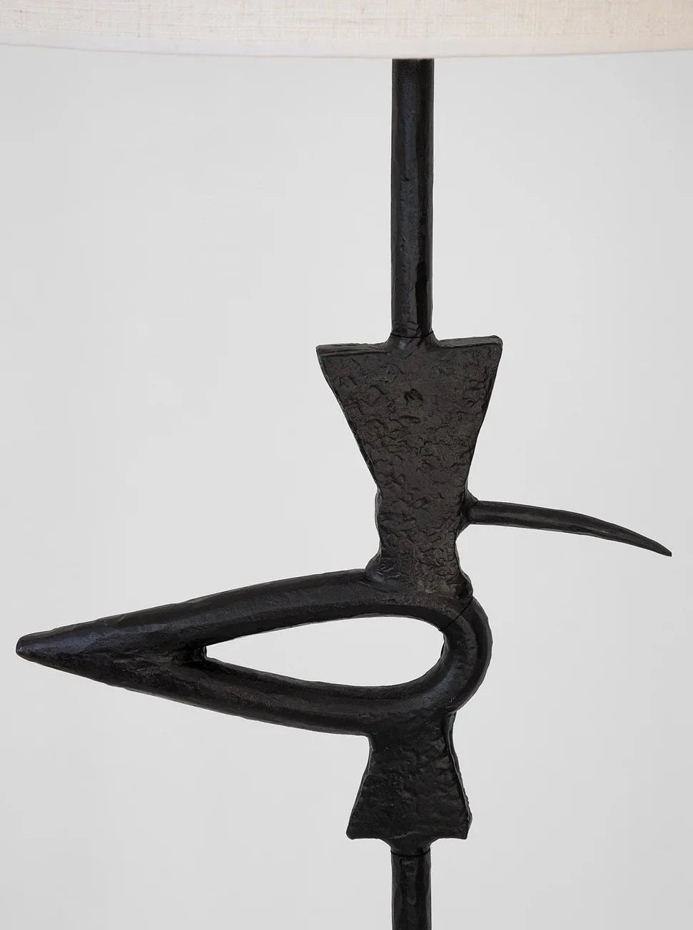 A close-up of the "Brejos" Floor Lamp by Barracuda Interiors shows its sculptural black metal base with abstract geometric and curved shapes, evoking a stylized creature—ideal for customizable lighting against a light gray background.