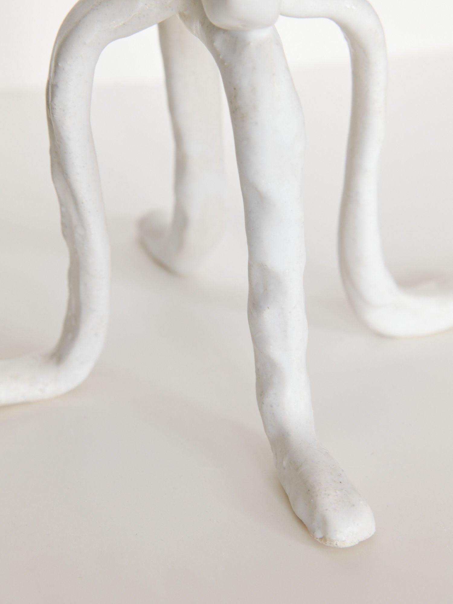 Close-up of Candleholder La Chose 2 by Claire Pain—white chamotte stoneware with four twisted, elongated legs, displayed on a smooth light surface. A unique artistic piece for distinctive home decor.
