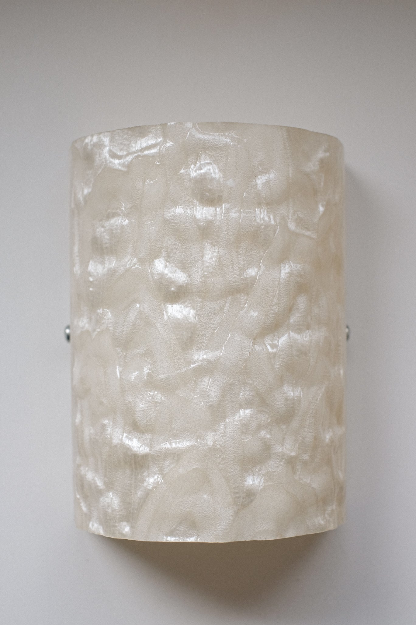 A close-up of the septembre studios Set of 2 Mother-of-pearl Wall Lamps, featuring a textured off-white, glossy wavy surface, evoking vintage style and mounted on a plain light-colored wall.