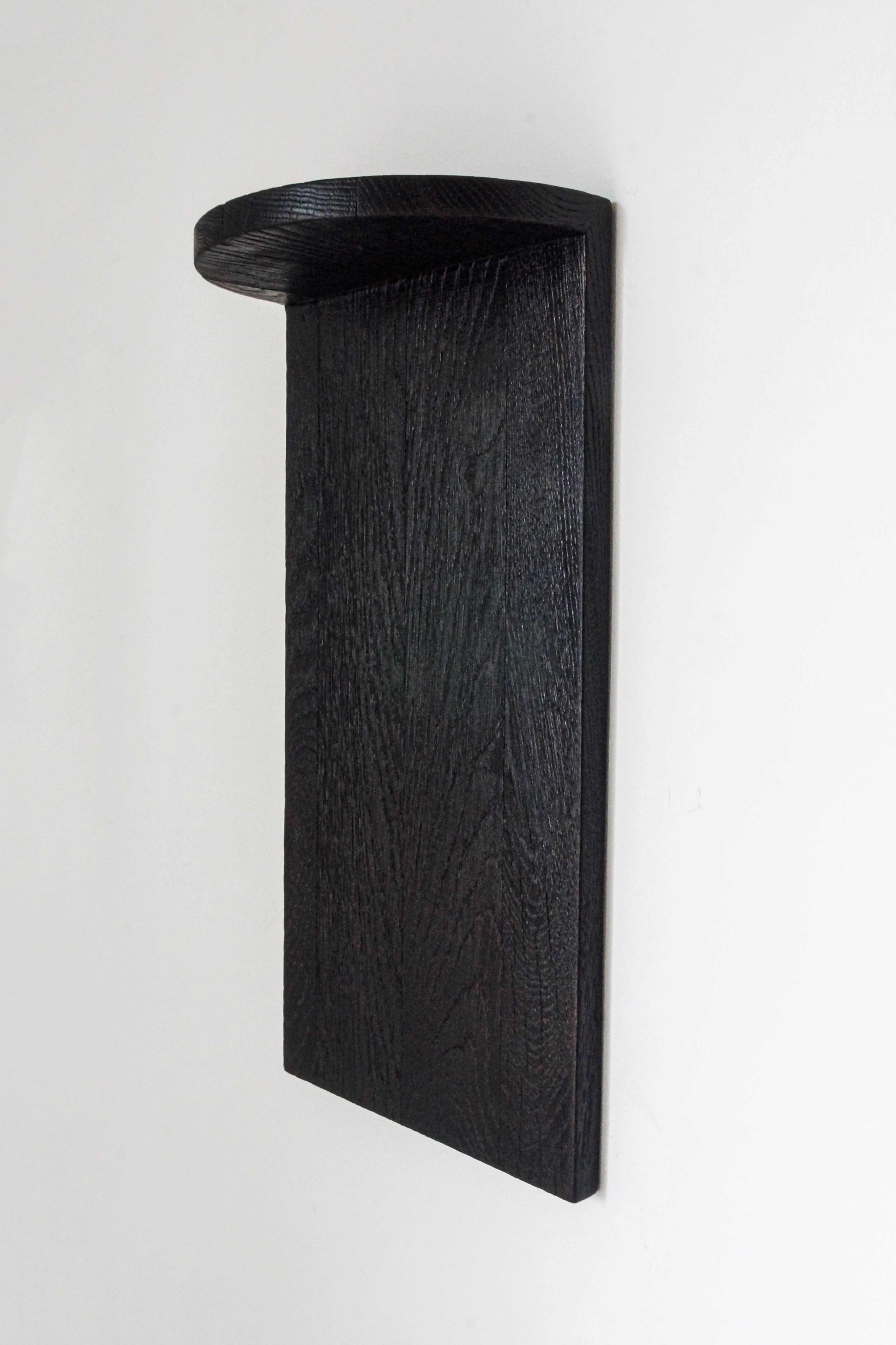 The Megaron - Minimalist Shelf in Wood (Small) by COSEINCORSO features a sleek, dark handcrafted solid oak design with a rectangular back panel and half-moon top shelf, shown mounted on a white wall.