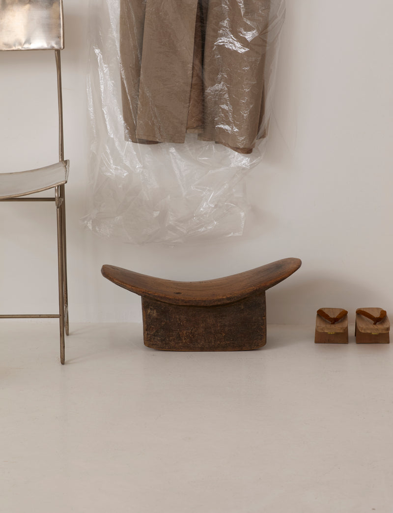 Mid-Century African Senufo Stool in Solid Wood — angled view on white floor with clothing