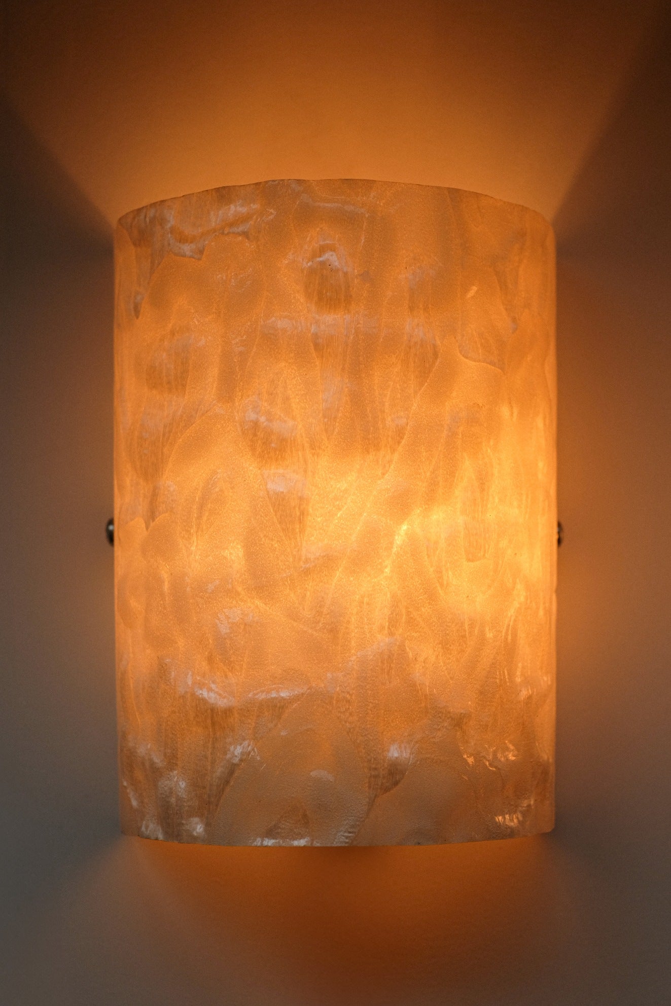 The Set of 2 Mother-of-pearl Wall Lamps by septembre studios features a textured cylindrical design that emits a warm amber glow, creating soft patterned shadows on your wall.