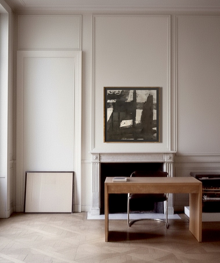 A minimalist office features a wooden desk, modern chair, and fireplace. Above the mantel hangs "Marblehead Harbor" Ink and Charcoal on Raw Canvas by Médecine; a large empty frame leans nearby. Light walls and herringbone wood floor complete the scene.