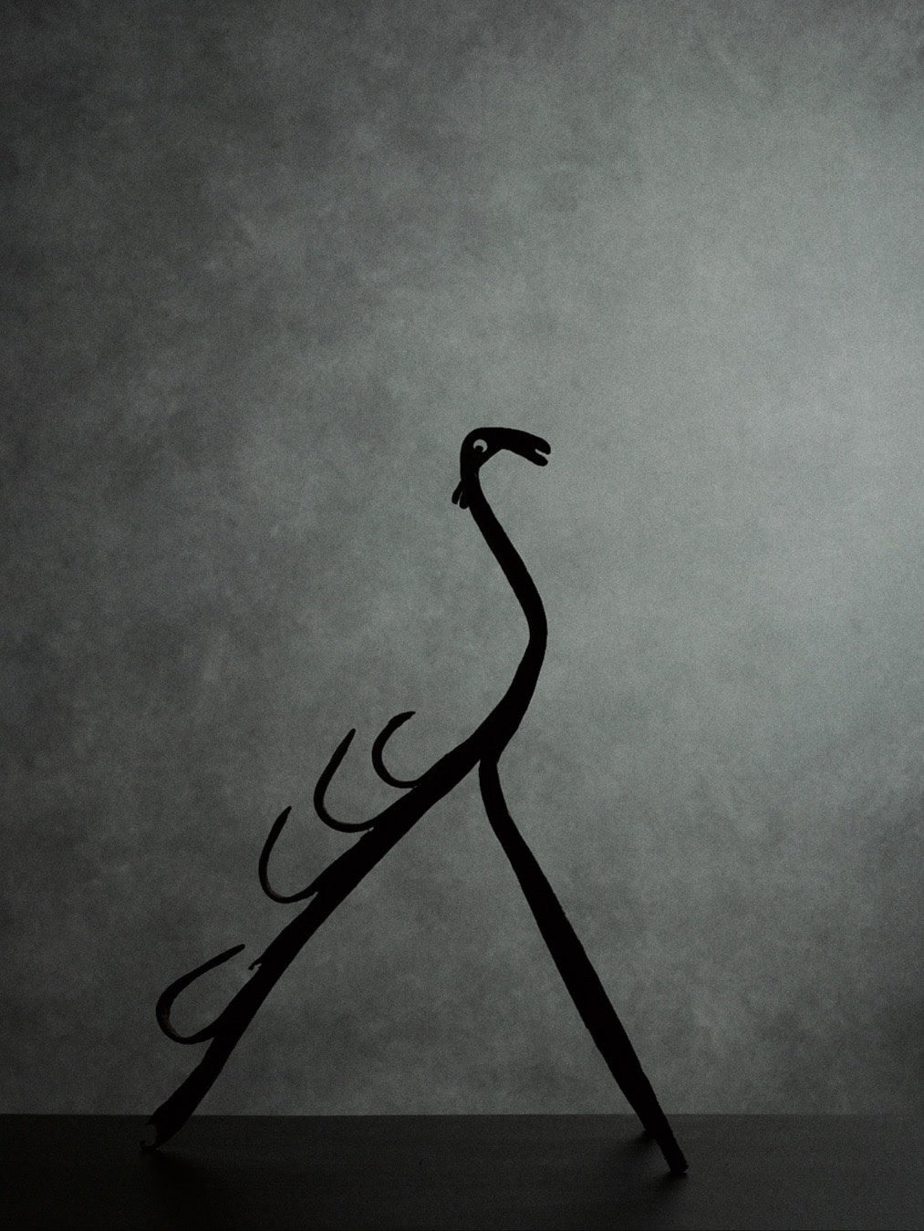 handcrafted iron sculpture with primal animal motifs — back view against gray background