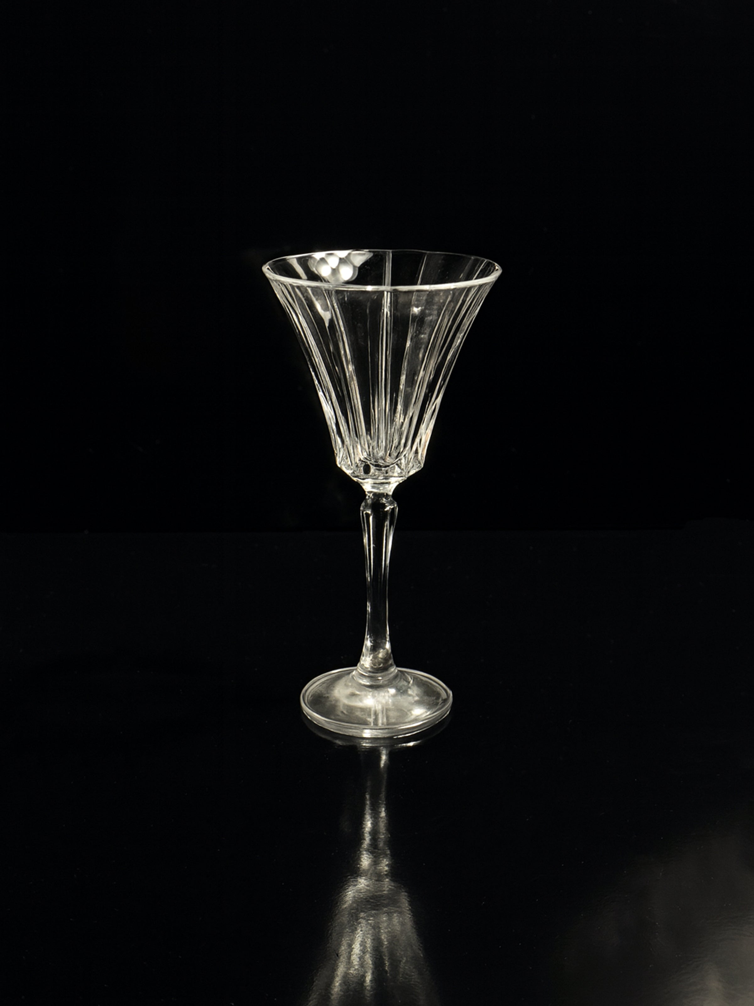 A Dodo Vintage Italian champagne and wine crystal goblet with a long stem stands on a reflective black surface against a solid background, exuding Art Deco elegance. Part of the Italian crystal sets and carafe collection.
