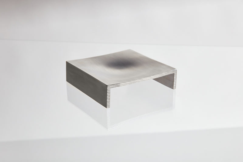 The LESORR Square Aluminum Vide-Poche, featuring a curved top and two short legs like a mini bridge, acts as a stylish small object holder on a glossy white background.