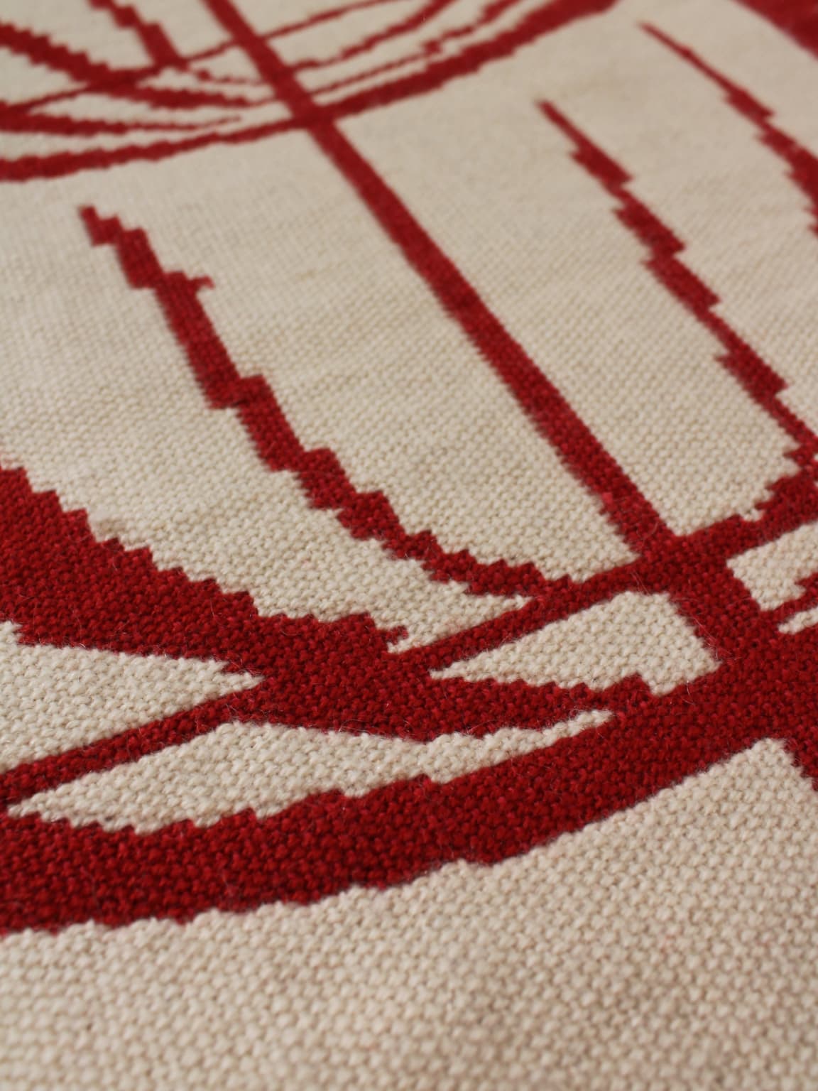 Close-up of the Vintage Stories Red Wool Wall Tapestry With Abstract Nature Motifs (72x180cm): beige wool fabric features pixelated red geometric shapes, creating a bold abstract nature motif on a neutral background.