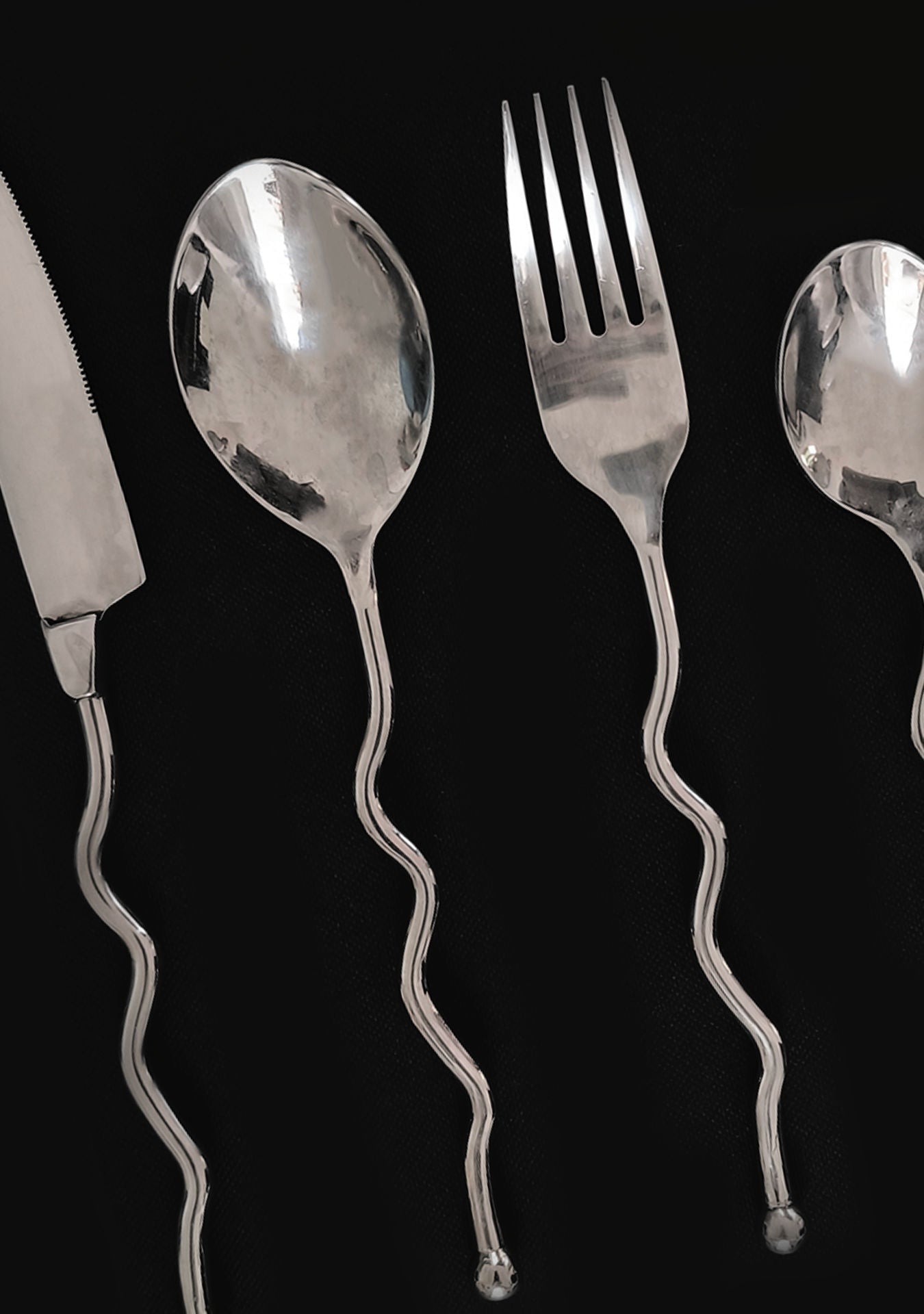 The Les Objoies Set of 4 Zig-zag Cutlery features a knife, spoon, fork, and teaspoon with unique wavy handles from a vintage collection, displayed on a black background.