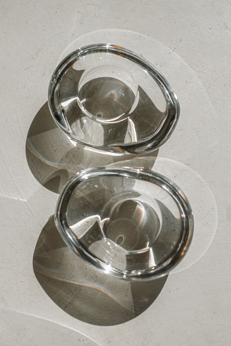 Two clear crystal candleholders casting elegant shadows on white surface