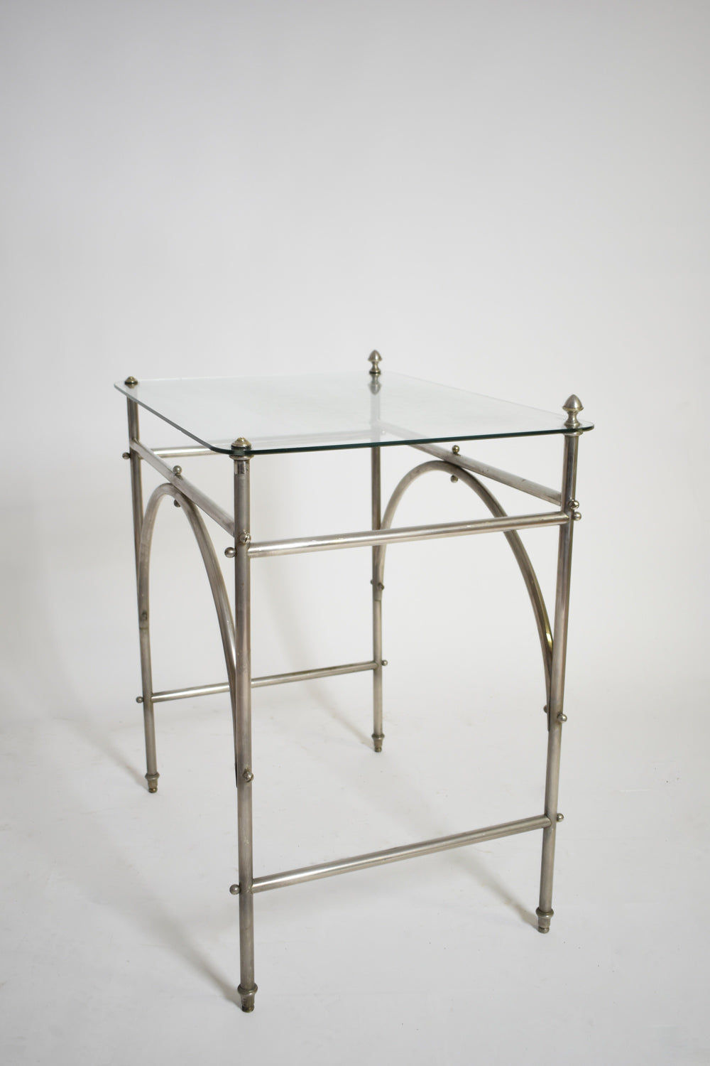 The Tubular Chrome Iron and Glass Table, 1920s by Barracuda Interiors features a square glass top, chrome iron frame with arched supports, and decorative finials—evoking classic 1920s style against a plain white background.