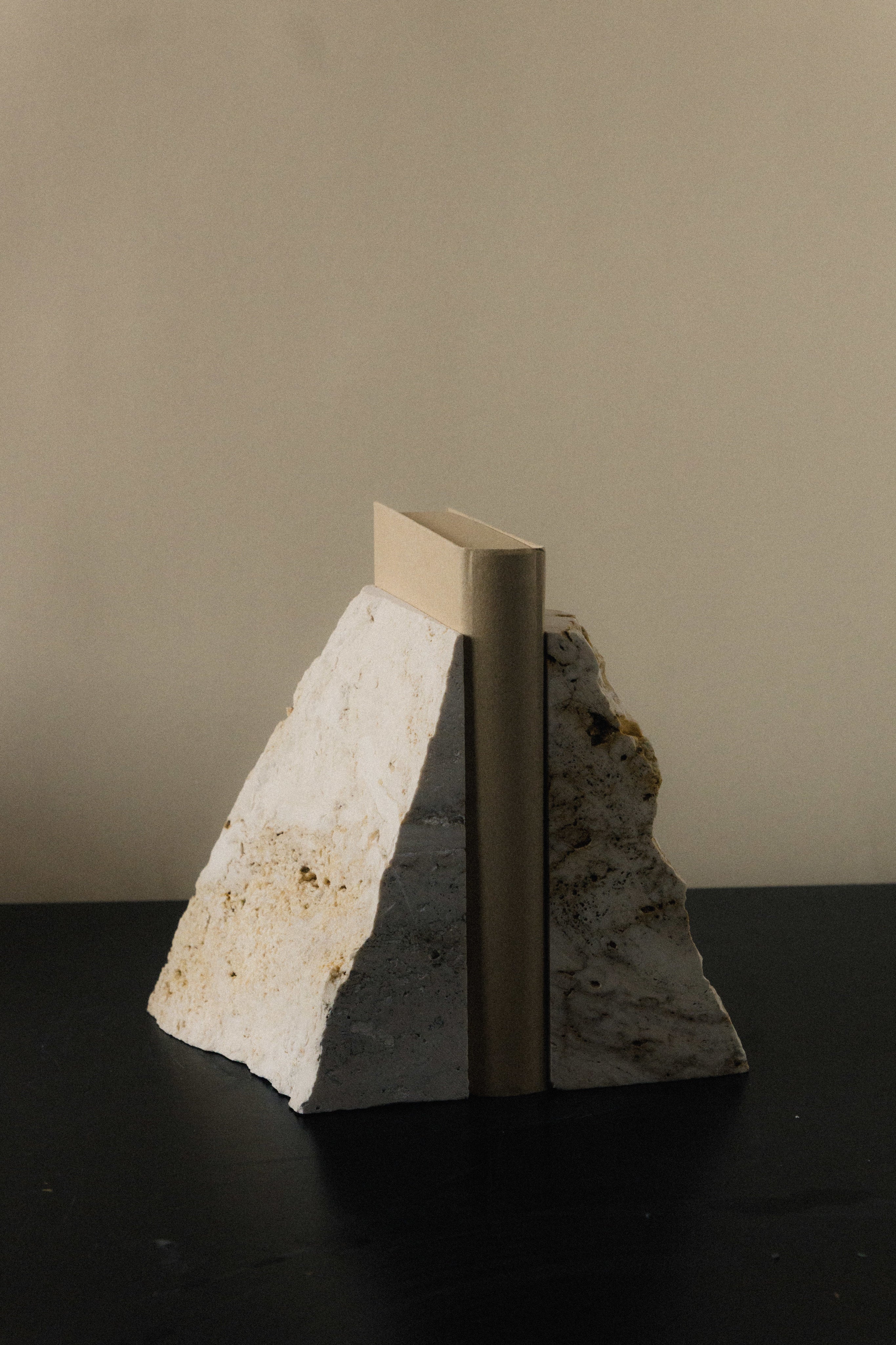 The Fragma Bookend III - Handmade Travertine Marble Bookend — angled view on dark table