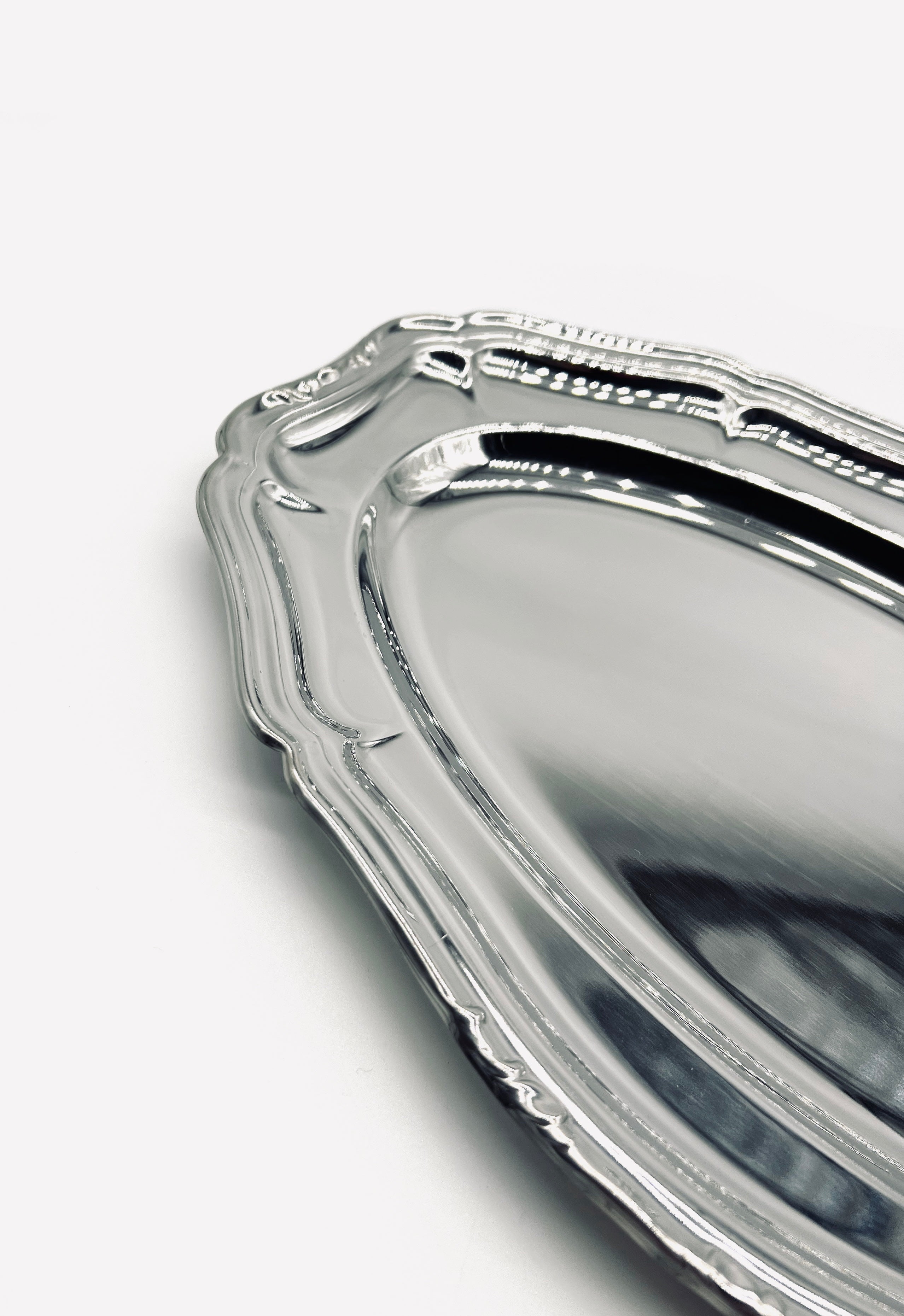 A close-up of the LA PARADE Medium serving dish showcases its ornate, vintage-inspired stainless steel with decorative edges and a reflective surface, evoking elegant 70s design on a white background. Only part of the dish is visible, highlighting its intricate border.