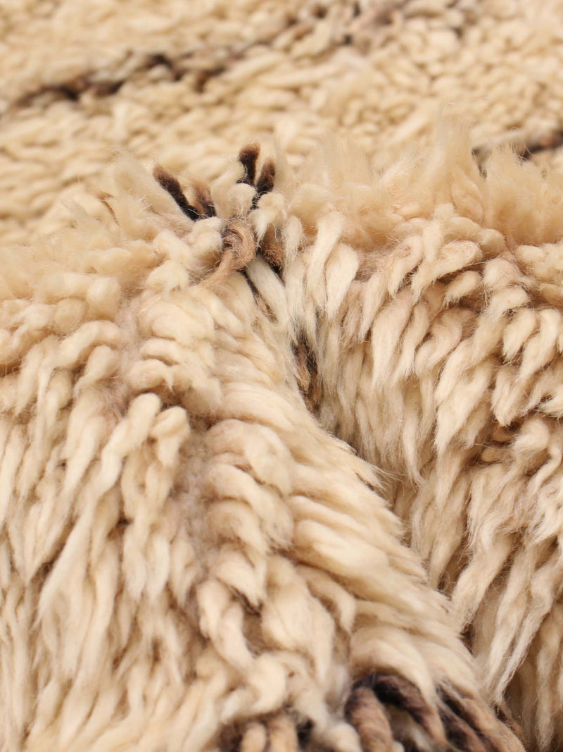 Close-up of the textured, cozy wool fibers in the Moroccan Berber Rug in Ivory (196 x 295 cm) by catalog:three, featuring cream-colored tones with a few darker brown strands for a vintage look.