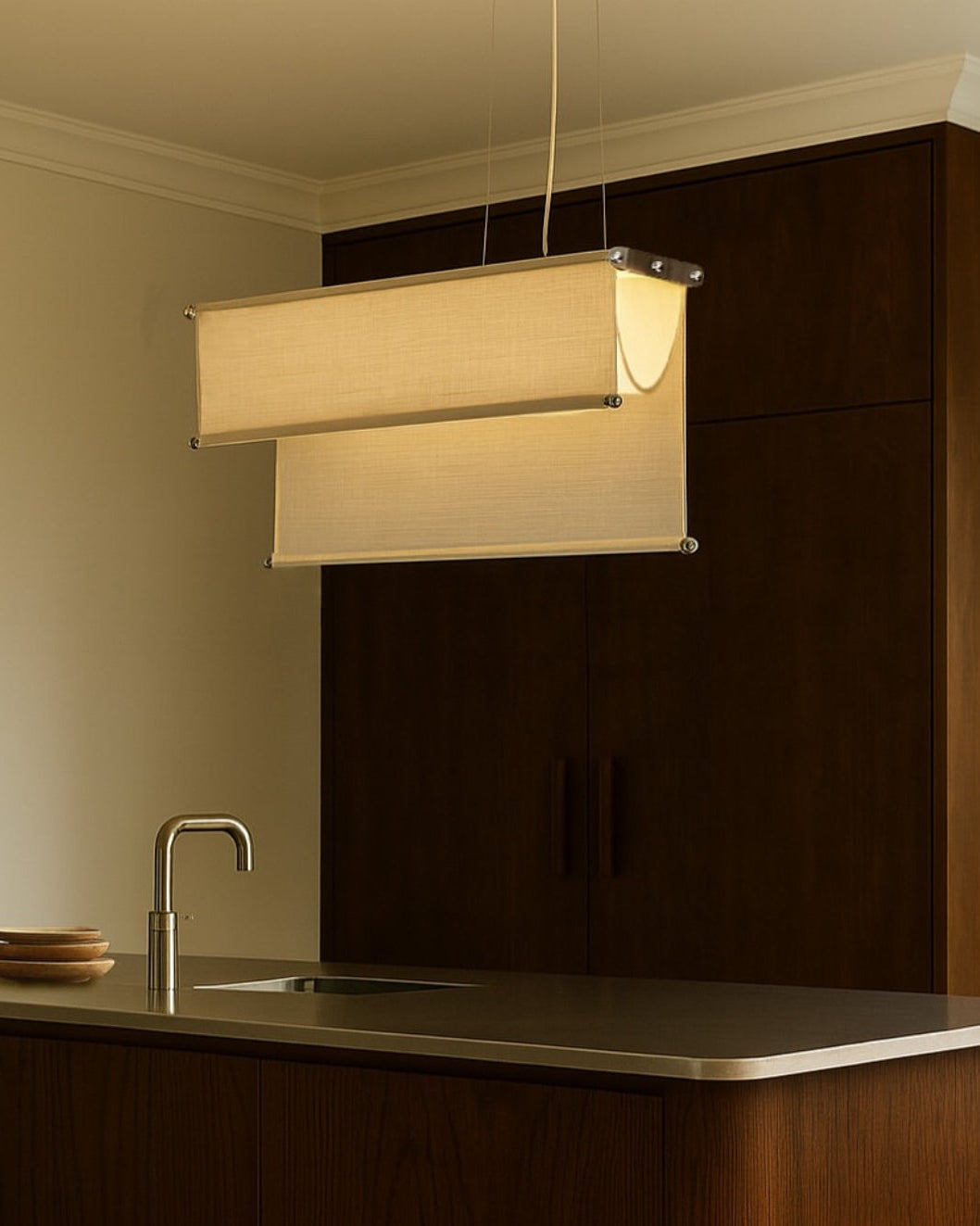 A modern kitchen with a dark wood cabinet, stainless steel sink, minimalist faucet, and the Caia Leifsdotter Vento Pendant—an adjustable light with two beige fabric shades—hanging above the counter.
