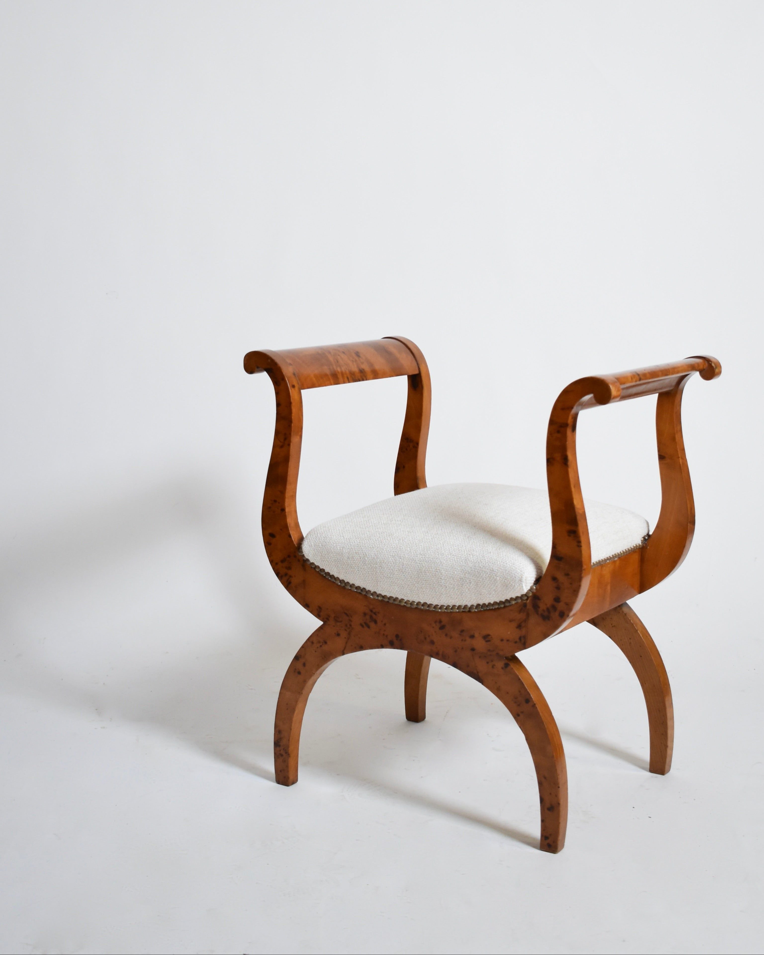 A pair of XIXth-century Walnut Curule Stools by Barracuda Interiors, featuring curved legs and armrests with light upholstered seats, in a classical design, set against a plain white background.