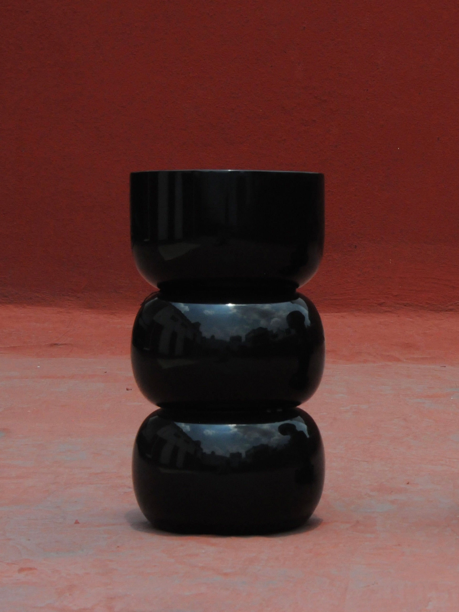 Chess' Stool convex in lacquer wood — front view against red wall