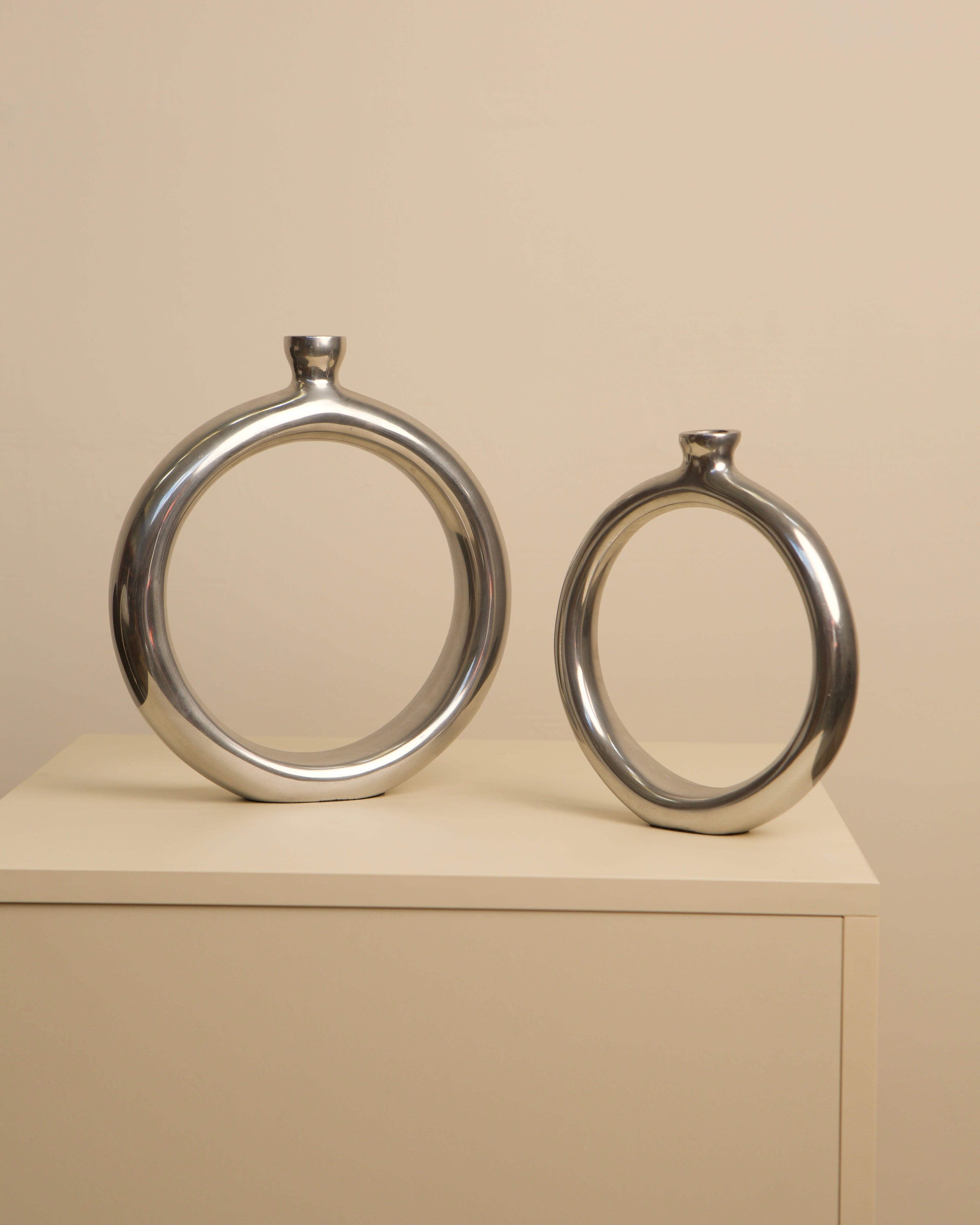 Pair of circular aluminum Italian vases displayed on beige cabinet