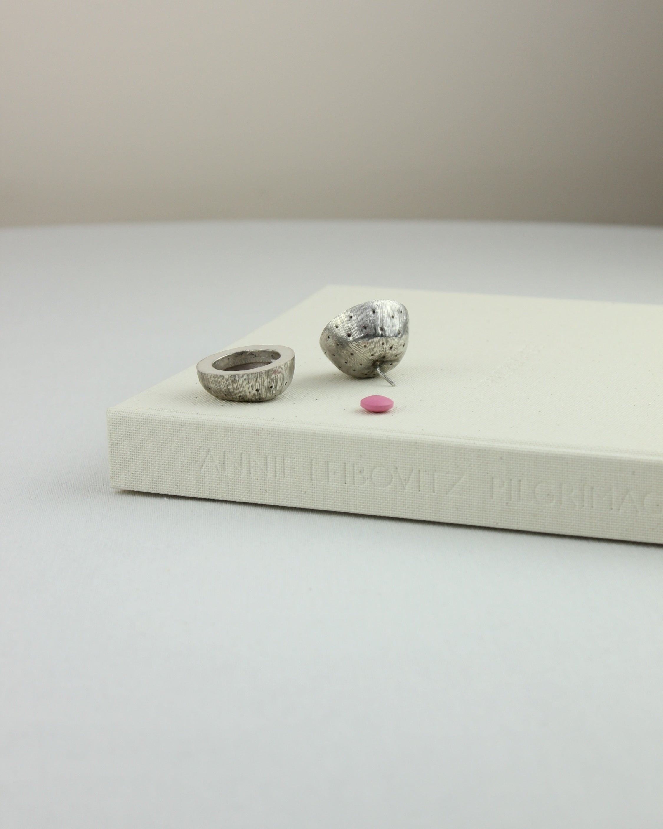 Silver Pillbox — positioned on a white book with pink pill