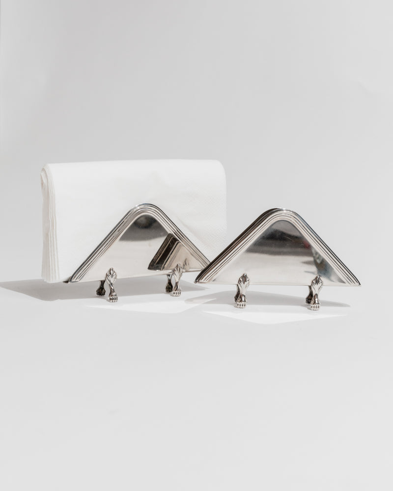 Two chrome triangular napkin holders with decorative feet, profile view