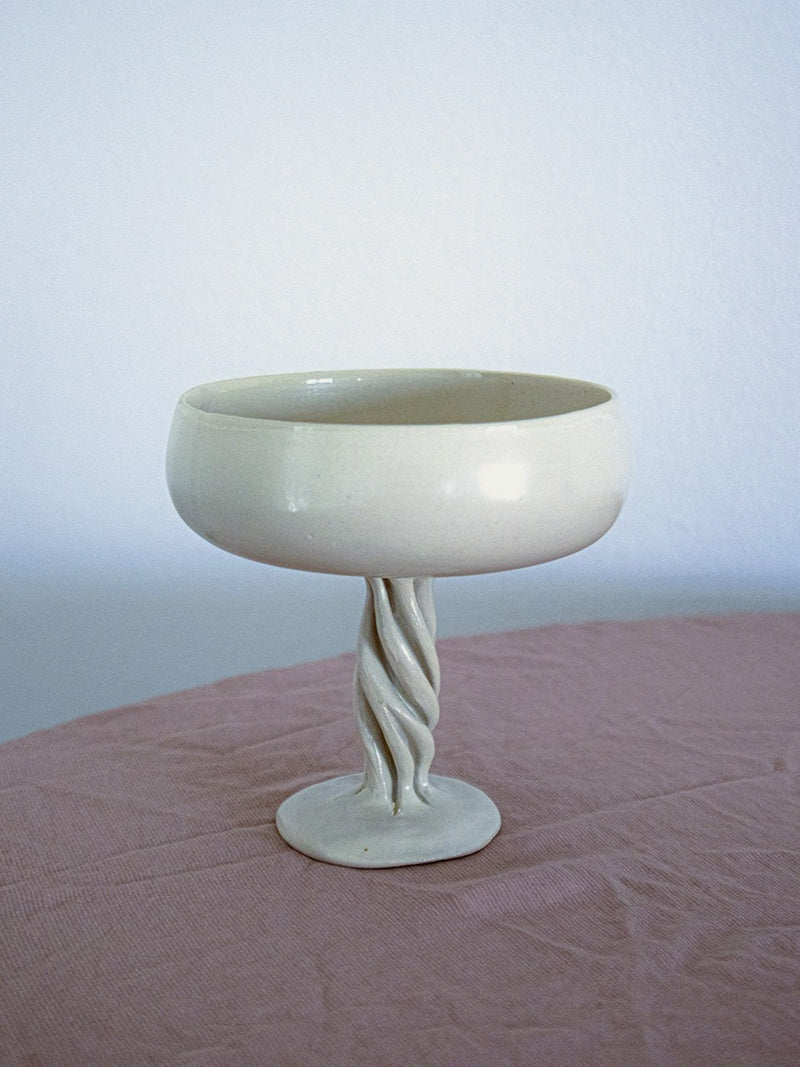 The Ceramic Champagne Coupe Contemporary by Anna Karountzou, a striking white bowl, is elegantly displayed on a pink surface.