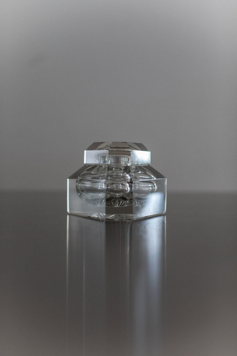 Clear glass perfume bottle with ornate stopper on reflective surface