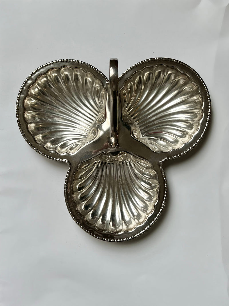 The Manushi Silver Club Shell Dish features three shell-shaped compartments joined together with a central decorative handle, displayed on a plain white background.