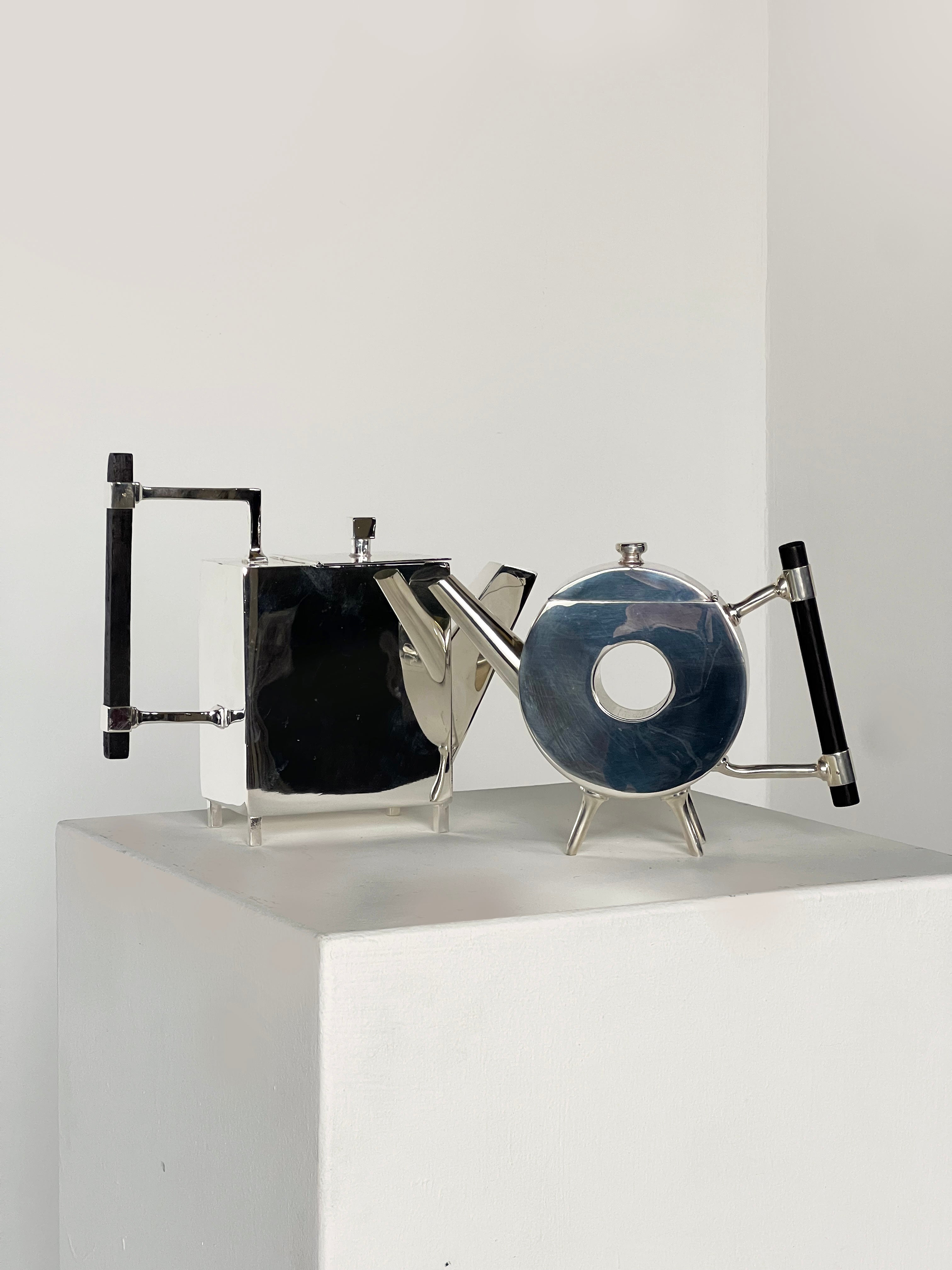 Two modern, geometric silver teapots are displayed: one is the Porter Studio Christopher Dresser Round Window Ornate Teapot; the other, a box-shaped vessel, resembles stylish Dixon & Sons silver-plated designs.