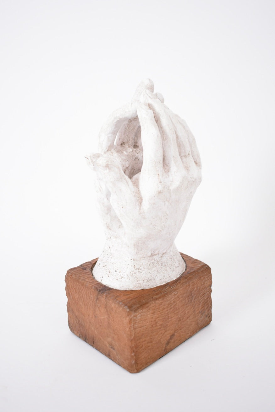 The Barracuda Interiors Rodin Style Plaster and Wood Sculpture, 1960s, features two white hands gently cupped together on a square wooden base, capturing vintage elegance against a plain white background.