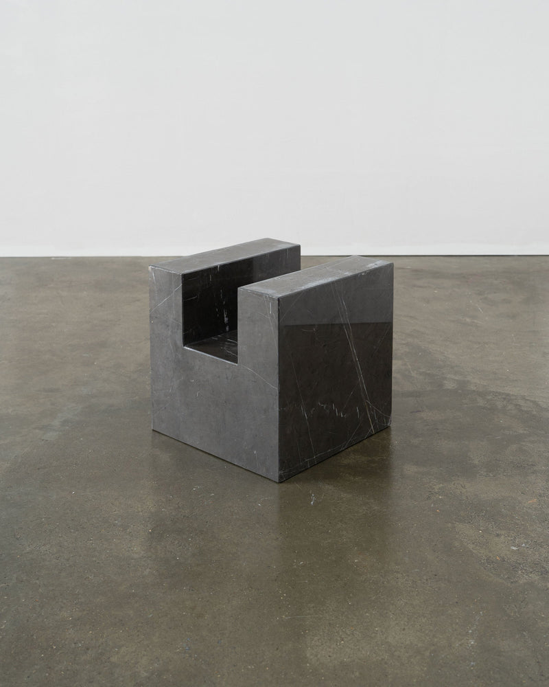 The Tom Bogle Postmodern Solid Marble Stool / Side Table features minimalist, rectangular lines and a dark marble finish, exuding elegance as it sits on a polished concrete floor against a plain wall.