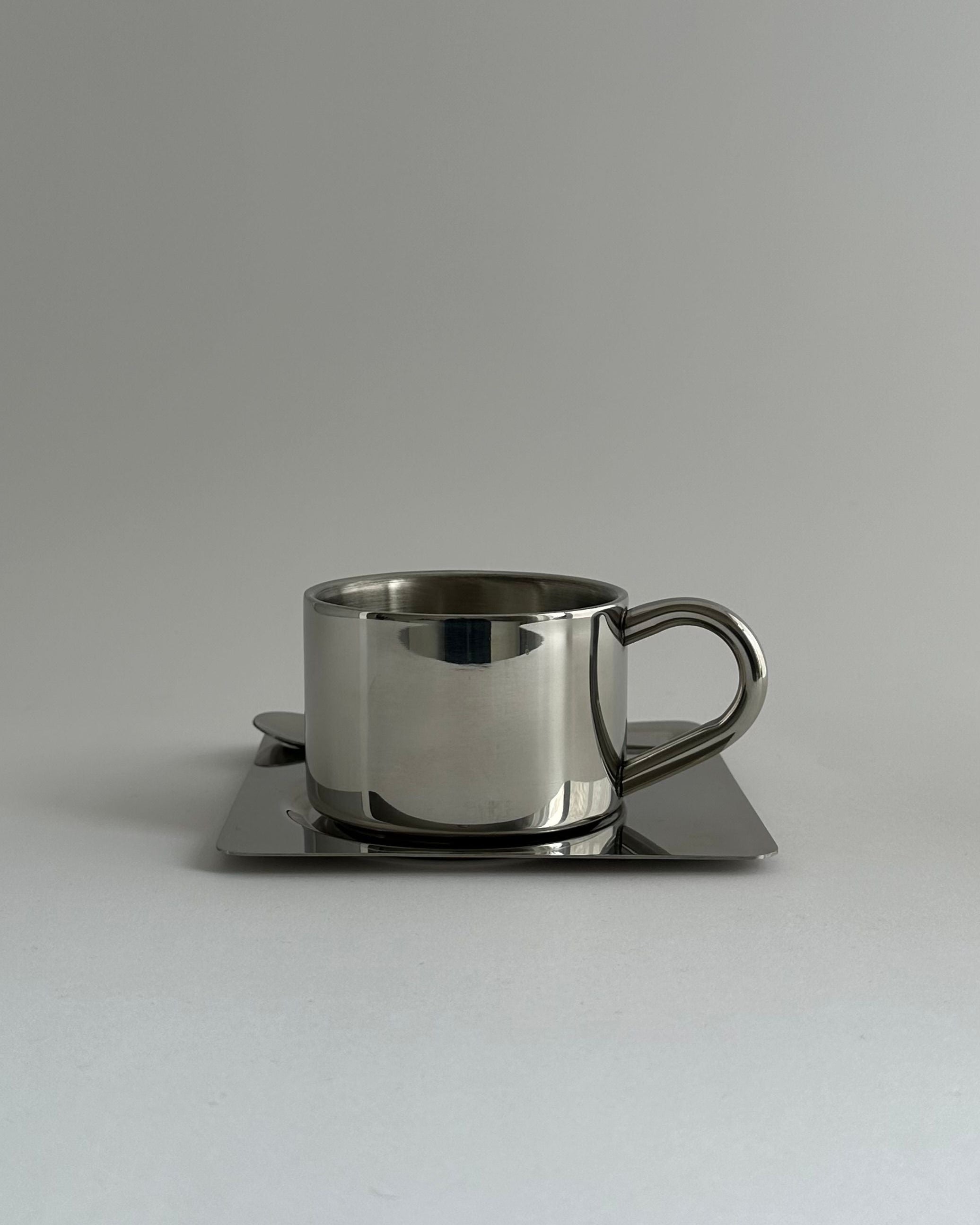 'HEDONISM' stainless steel cup with saucer — close-up