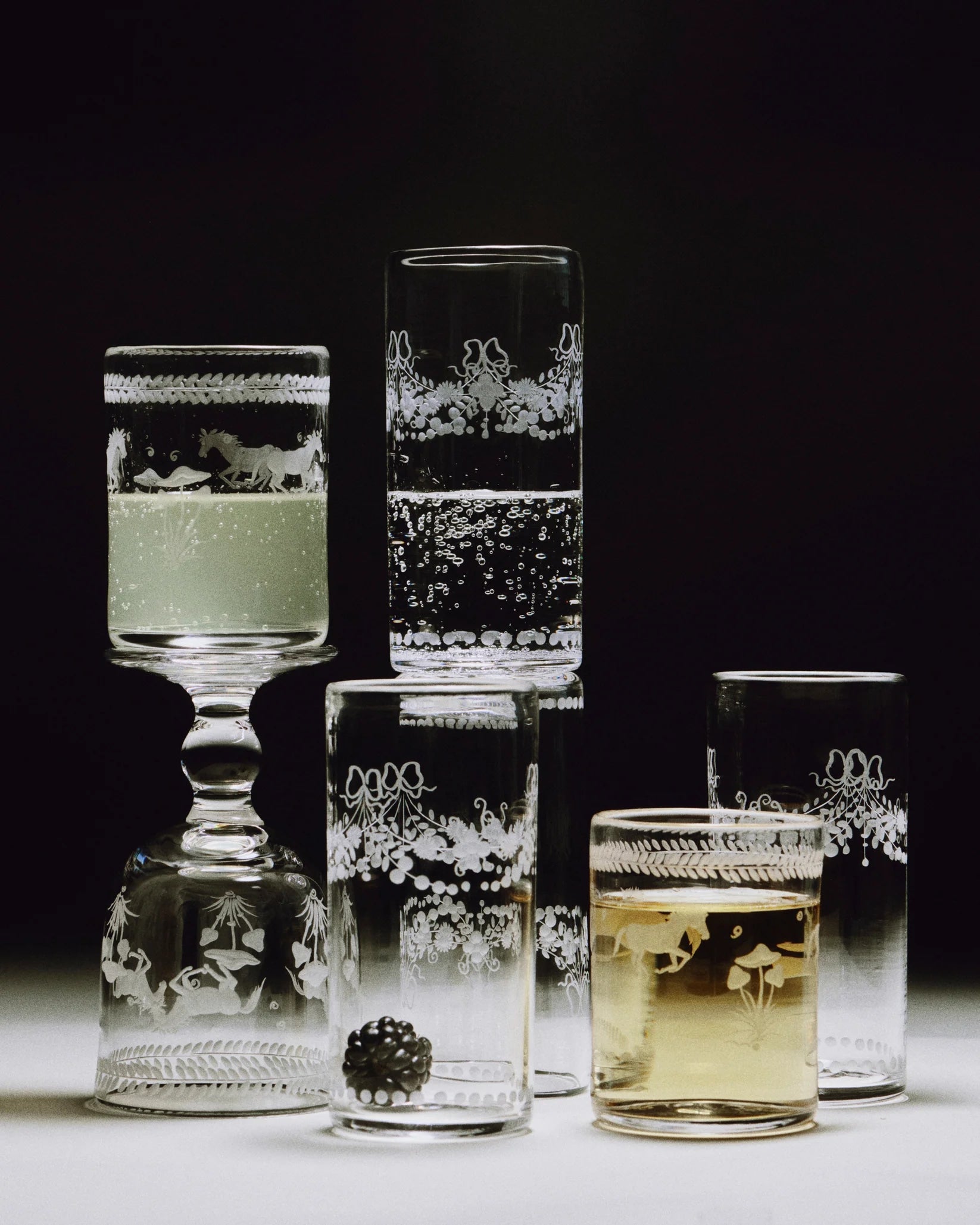 Barbro Water Glass - Set of four — arranged with various drinks on dark background