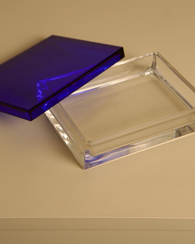 The Italian Box in Transparent and Blue Crystal by Duccio Di Segna 80's from Treaptyque features a rectangular form with a blue-tinted lid, partially open on a beige surface, reflecting iconic 1980s Italian design.