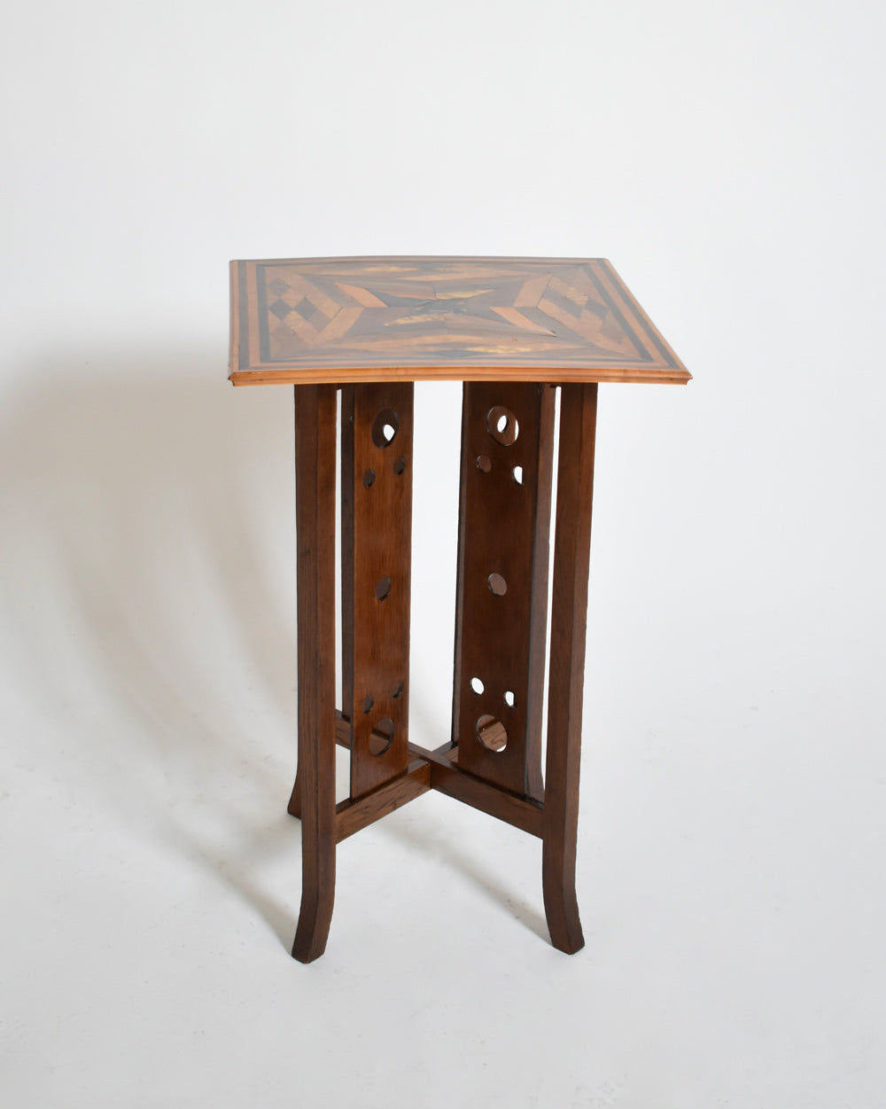 Barracuda Interiors’ Geometric Marquetry Side Table, 1920s, features a square top with bold geometric marquetry and circular cut-out panel legs, showcased against a white background.