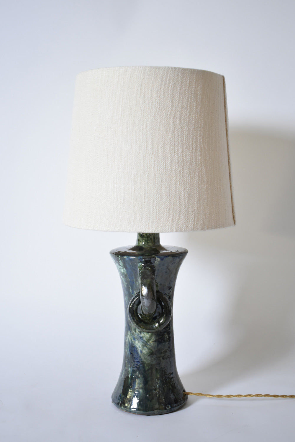 The "Kasaï" Blue & Green Ceramic Lamp by Barracuda Interiors features a textured base, white fabric shade, and gold power cord on the right. Made in Portugal, it is shown on a plain white background.