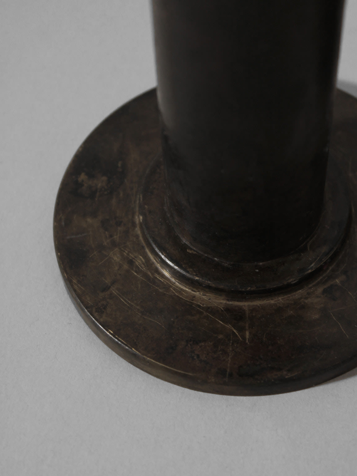 A close-up of the worn base of a dark, cylindrical iron object on a light gray surface, suggesting the 1970s Pair of Brutalist Massive Iron Candle Holders by Vintage Stories.