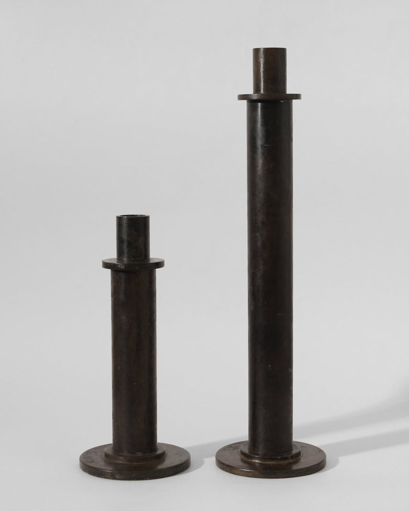 The Pair of Brutalist Massive Iron Candle Holders by Vintage Stories, 1970s, features two upright iron cylinders of different heights with round bases and flat top discs, evoking vintage German candle holder design.