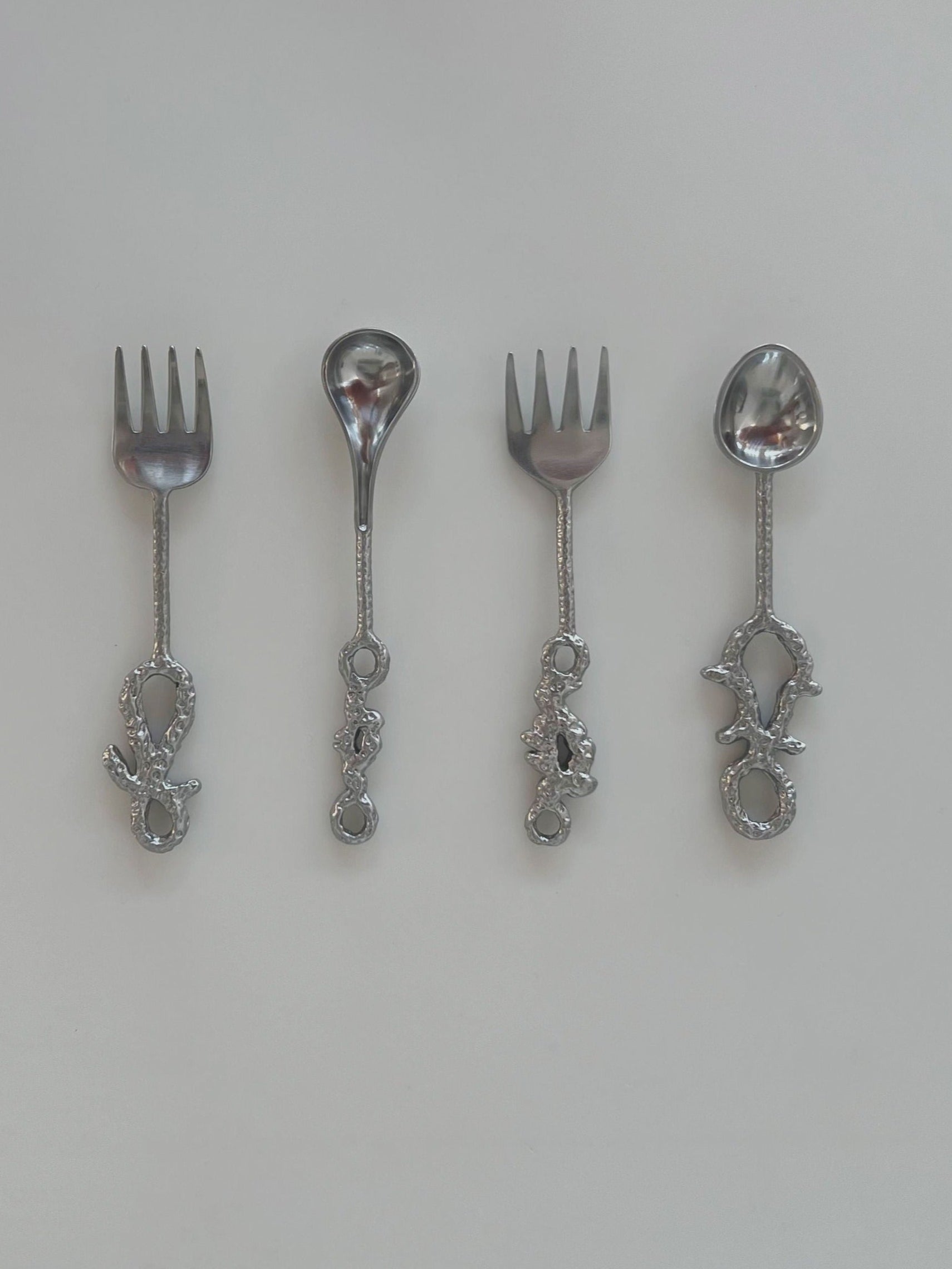 Two silver forks and two silver spoons on a light gray background