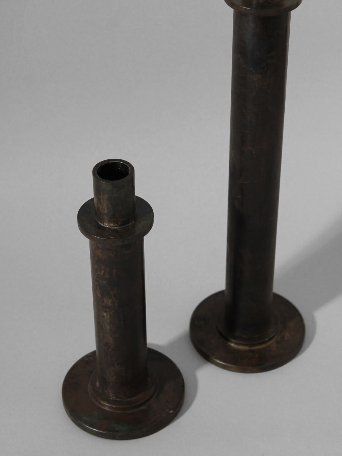 A Pair of Brutalist Massive Iron Candle Holders by Vintage Stories (1970s) stand on a light grey surface, their tall, cylindrical forms and industrial design evoking a vintage aesthetic. The image is shot from above.