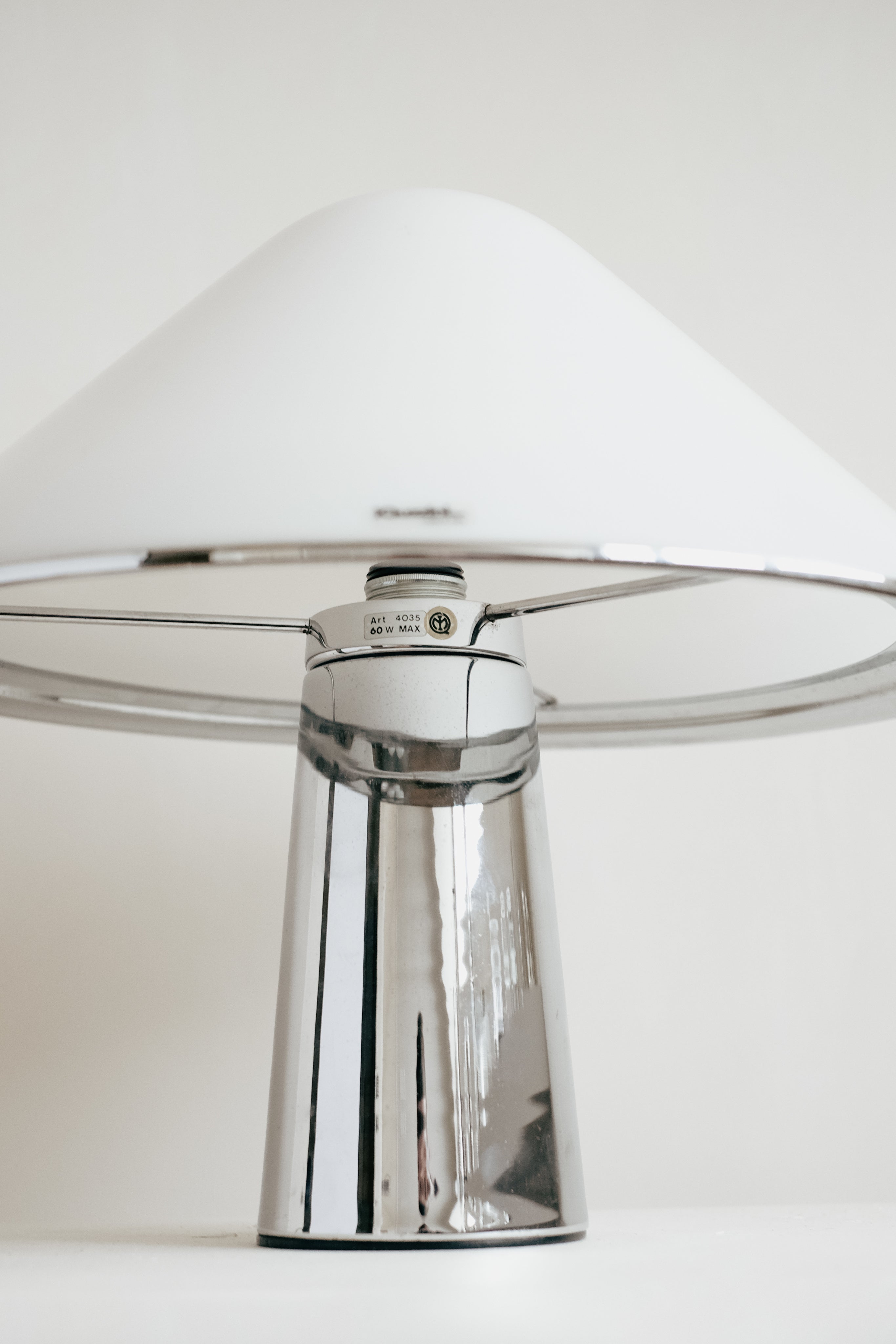 The Harvey Guzzini Elpis Table Lamp by septembre studios features a shiny metallic base and large white dome shade, inspired by Luigi Massoni's iconic design, and is set against a plain light background.