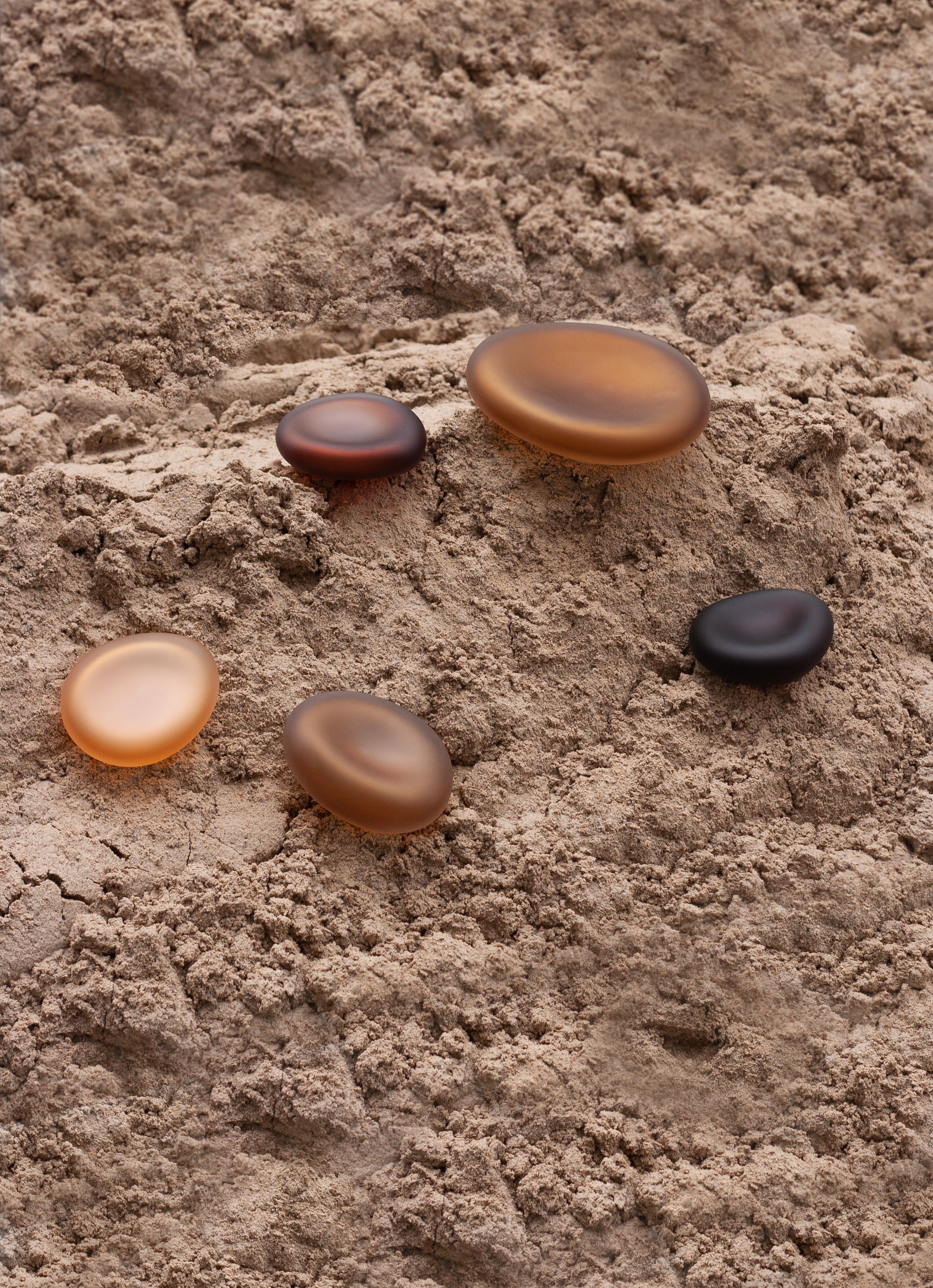 Glass Sculptures SEAGLASS | color deep amber — arranged on textured sandy surface