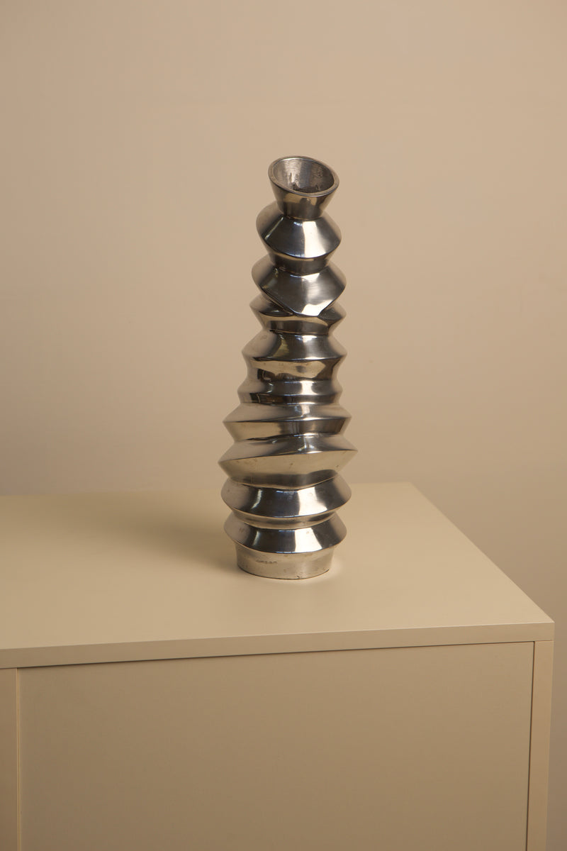 Sculptural aluminum vase with stacked disc design on shelf