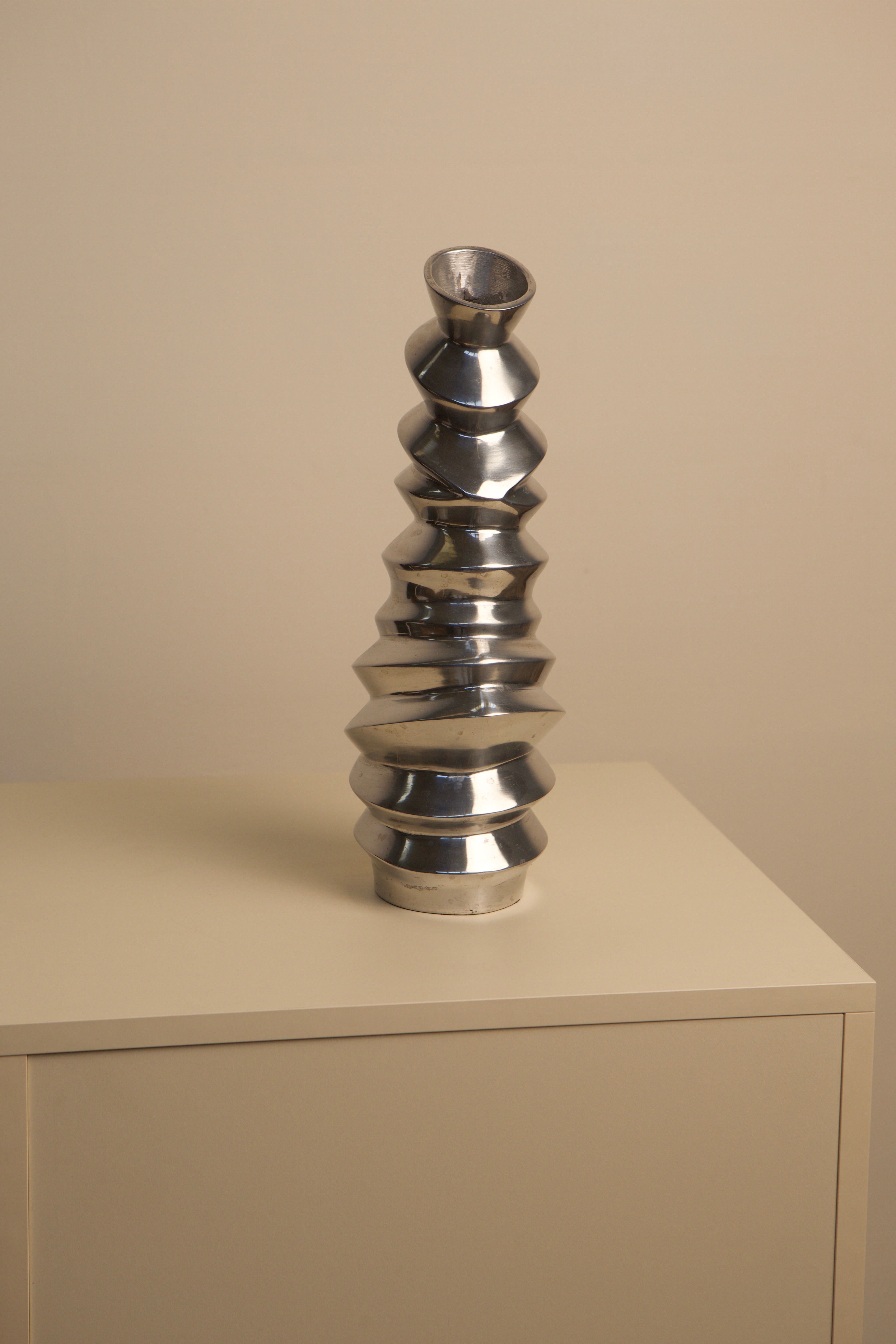 Sculptural aluminum vase with stacked disc design on shelf